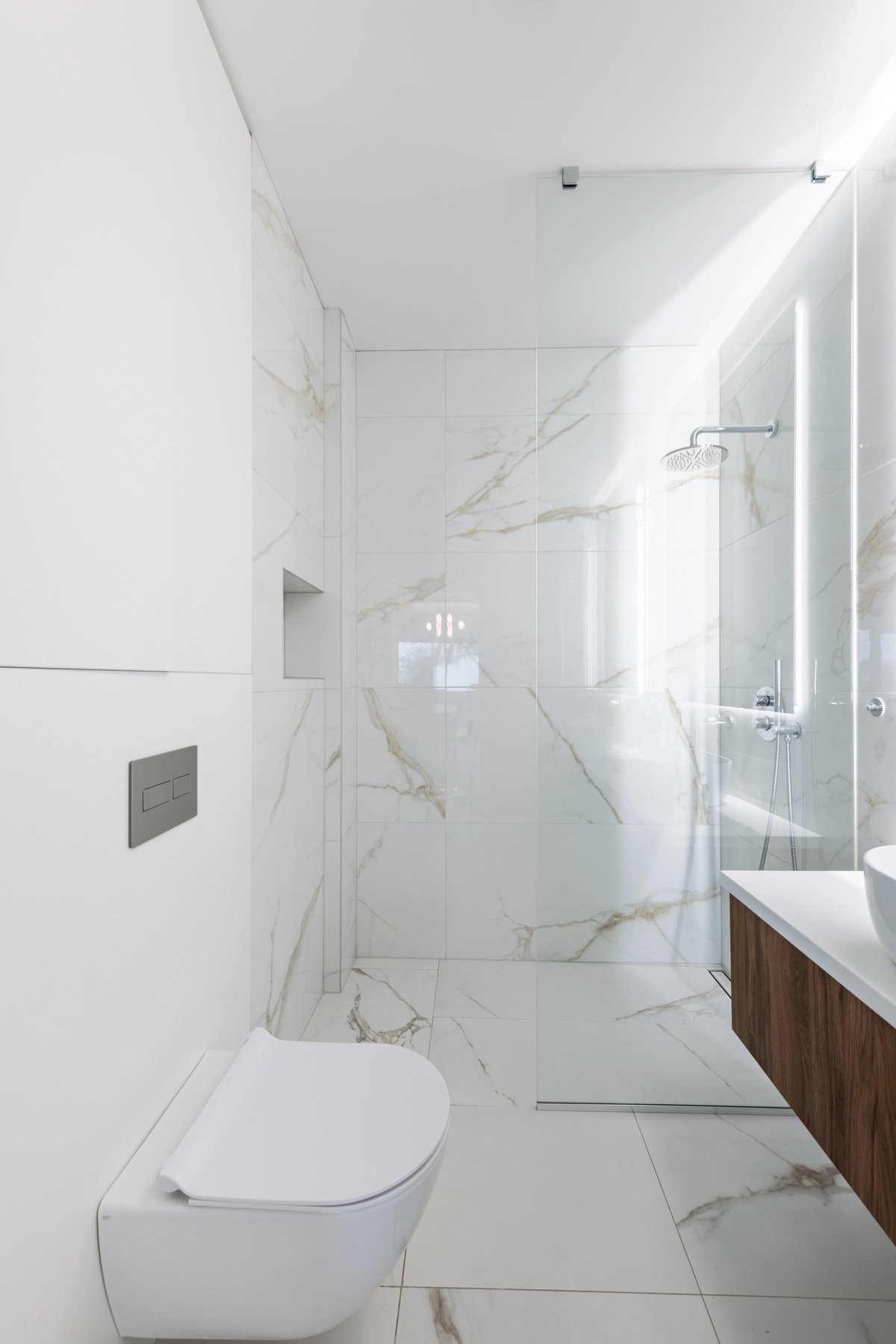 Bright modern bathroom with white marble tiles and frameless walk-in shower